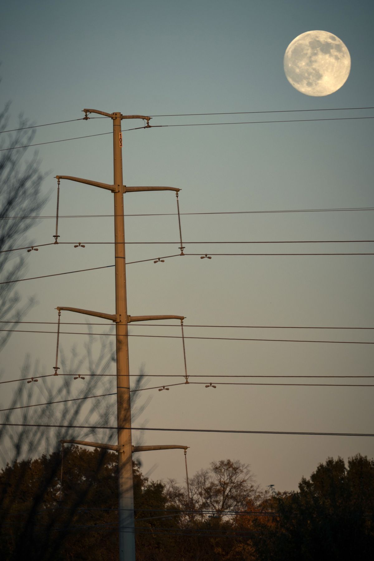 Full moon rising over power lines at dusk