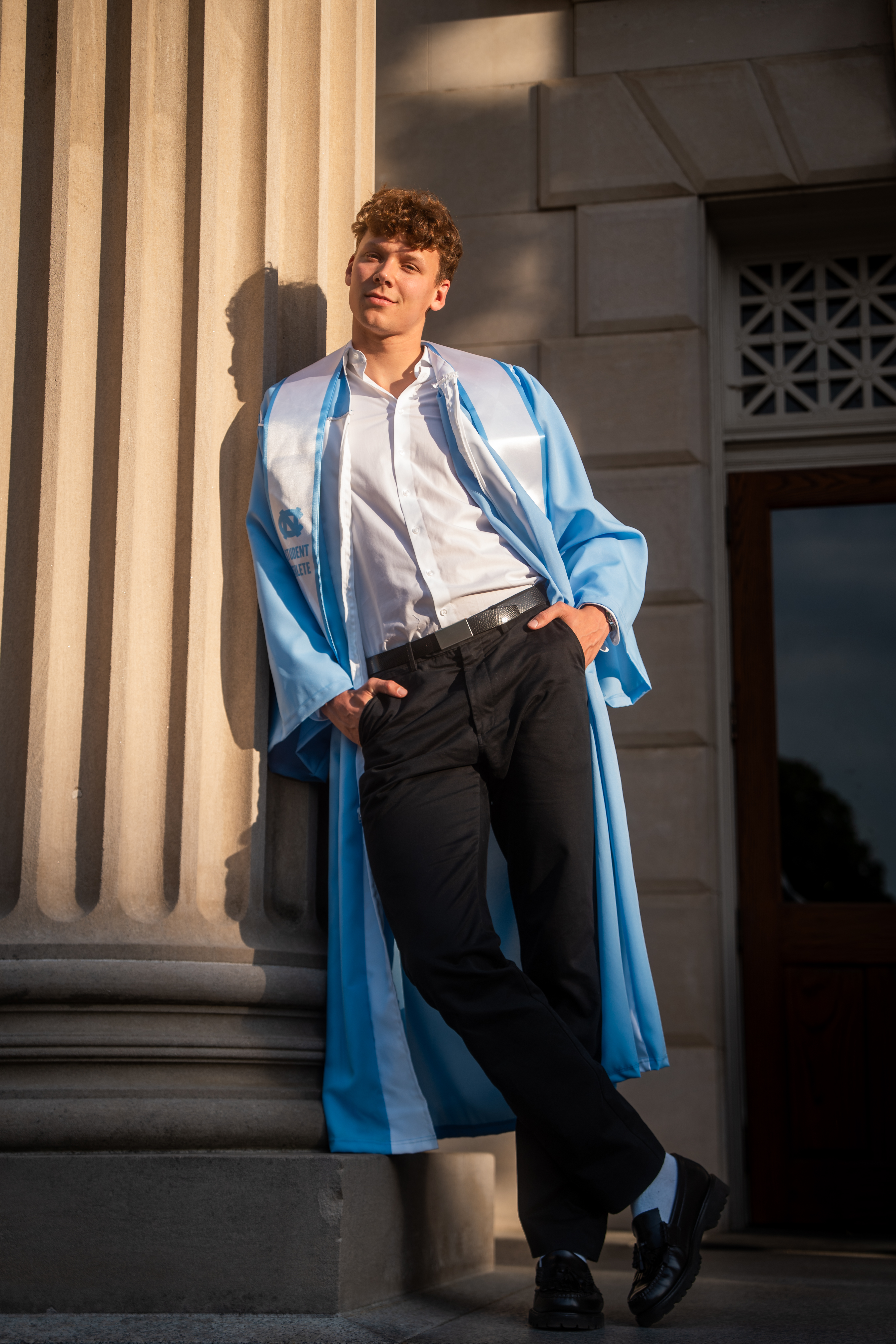 UNC graduate leaning against column in golden hour light